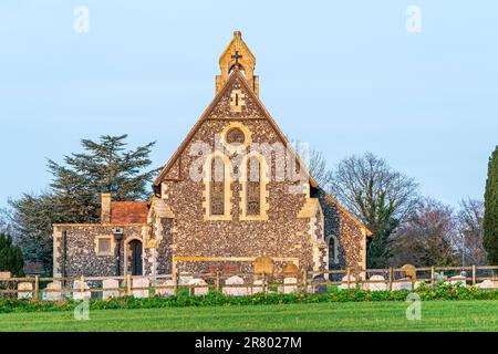 The Gothic Revival style church of St Mary at Reculver, with its walls of knapped flint lit-up by the sunrise (unseen). Nave wall against a blue sky. Stock Photo