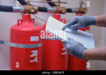 The inspector of fire security is using his notepad to jot down notes as he checks the fire extinguishers within the building. Stock Photo