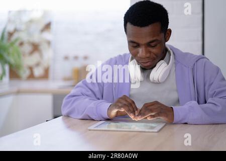 Black man using digital tablet on kitchen at home, working office work remotely typing text, African american freelancer using notepad computer Stock Photo