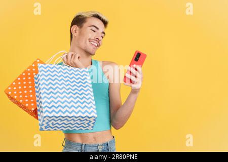 Happy gay man using the mobile while holing shopping bags Stock Photo