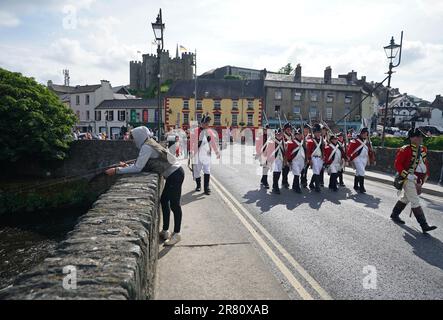 A man fishes on the bridge as behind him re-enactors recreate the battle of Enniscorthy Bridge in Enniscorthy, Co Wexford to mark the 225th anniversary of the 1798 rebellion between the United Irish men and the forces of the Crown. Picture date: Sunday June 18, 2023. Stock Photo