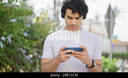 Young latin man watching video on smartphone wearing headphones at park Stock Photo