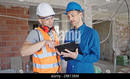 Two men builder and architect writing document speaking at construction site Stock Photo