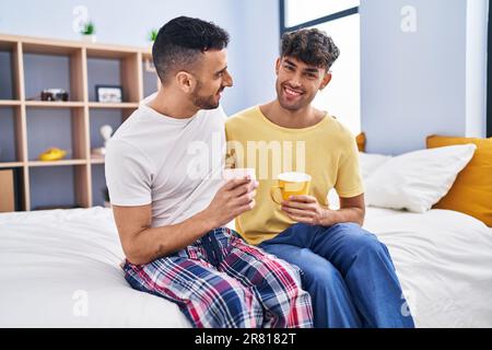 Two man couple drinking coffee sitting on bed at bedroom Stock Photo