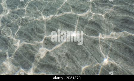 glare of sun plays on sandy bottom in shallow water. Top view on sandy seabed in shallow water with diagonal lines of sand and sun glare on its surfac Stock Photo