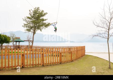 Teenage teen girl bungee flying in rope amusement park. Climbing harness equipment, green sports safety helmet. Hanging obstacle course. Kids children Stock Photo