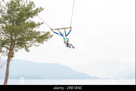 Teenage teen girl bungee flying in rope amusement park. Climbing harness equipment, green sports safety helmet. Hanging obstacle course. Kids children Stock Photo