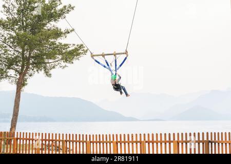 Teenage teen girl bungee flying in rope amusement park. Climbing harness equipment, green sports safety helmet. Hanging obstacle course. Kids children Stock Photo