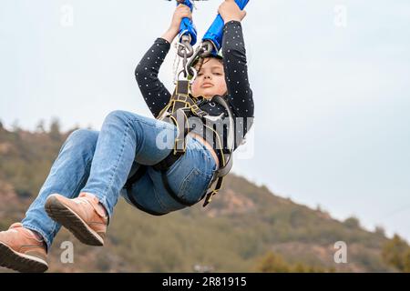 Teenage teen girl bungee flying in rope amusement park. Climbing harness equipment, green sports safety helmet. Hanging obstacle course. Kids children Stock Photo