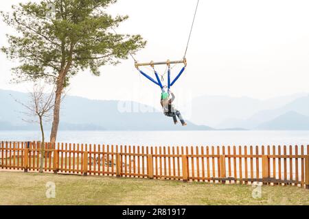 Teenage teen girl bungee flying in rope amusement park. Climbing harness equipment, green sports safety helmet. Hanging obstacle course. Kids children Stock Photo