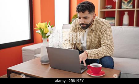 Young hispanic man using laptop drinking coffee at h Stock Photo