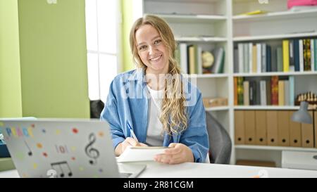 Young blonde woman student using laptop writing notes at library university Stock Photo