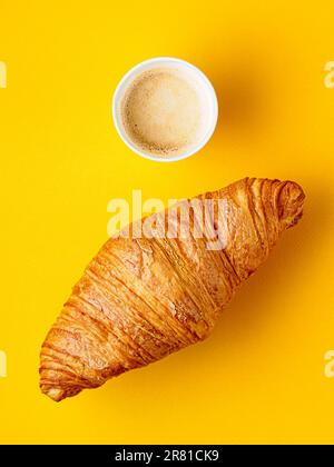 Top view on paper cup of coffee and croissant on yellow background. Breakfast concept. Stock Photo