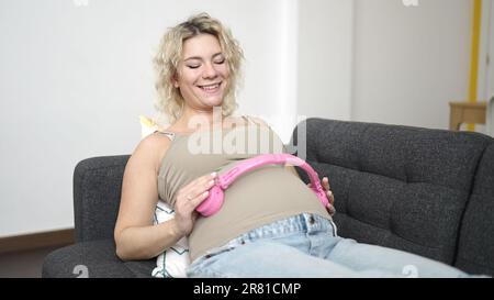 Young pregnant woman smiling confident putting headphones on belly at home Stock Photo