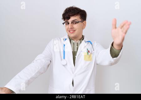 Young non binary man wearing doctor uniform and stethoscope looking at the camera smiling with open arms for hug. cheerful expression embracing happin Stock Photo
