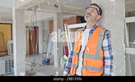 Middle age man builder tired taking out hardhat at construction site Stock Photo