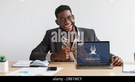 Young black man wearing eyeglasses working on laptop, using chatbot Stock Photo