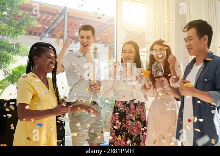Joyful friends dancing and drinking under falling confetti Stock Photo