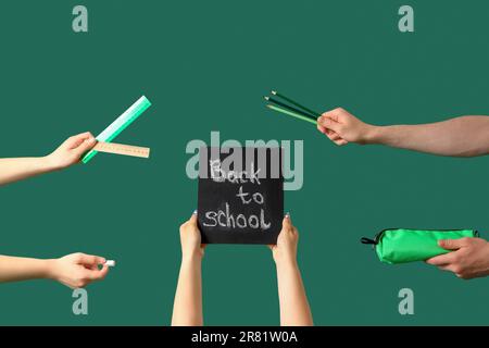 People holding chalkboard with text BACK TO SCHOOL and stationery on green background Stock Photo