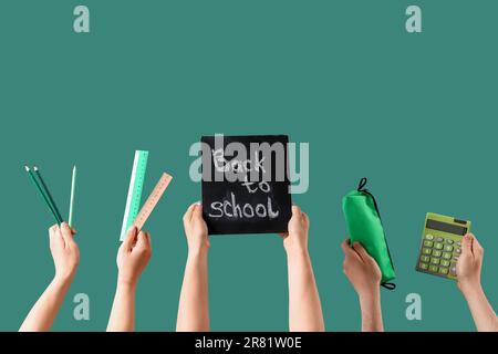 People holding chalkboard with text BACK TO SCHOOL and stationery on green background Stock Photo