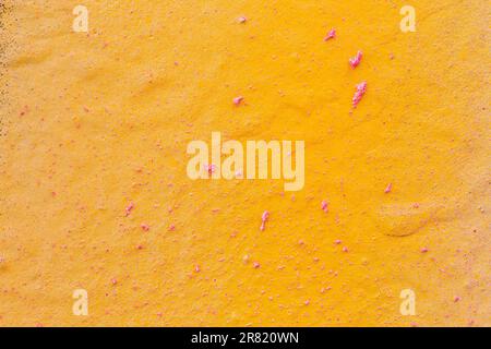 Close-up of a spray painted yellow orange wall with pink splashes. Abstract full frame textured grunge graffiti background with copy space. Stock Photo