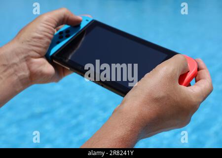 Man playing game on handheld console in swimming pool, selective focus on hand. Summer leisure on beach resort Stock Photo