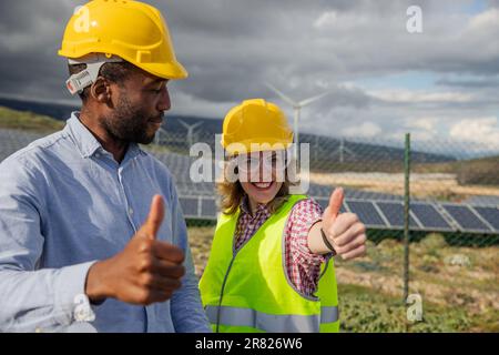 Two satisfied engineers in a solar power plant at work show the thumbs up, multi ethnic group Stock Photo