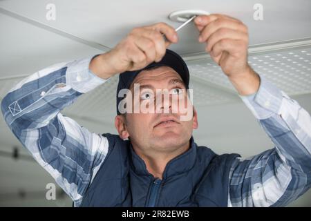 worker fixes the lamp to the ceiling with a screwdriver Stock Photo