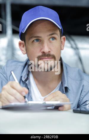 Smiling mechanic taking notes on clipboard while inspecting engine of ...