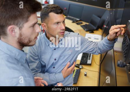 two male technicians looking at computor monitor in control center Stock Photo