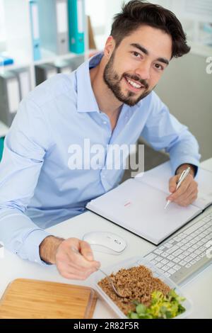 funny surprised office employee eating food while working Stock Photo