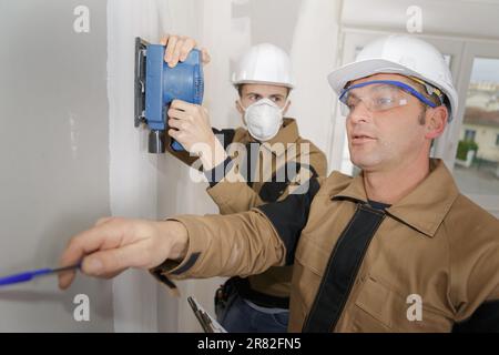 young builder in hardhat sanding wall indoors Stock Photo
