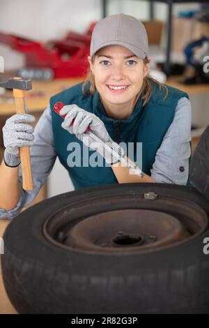 female mechanic using a hammer and chisel on a tyre Stock Photo