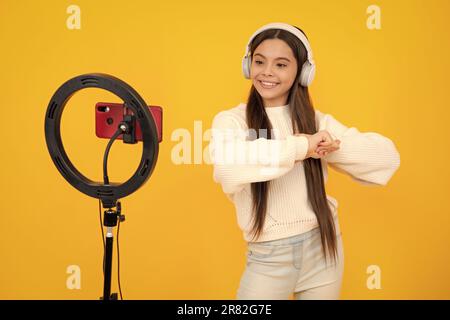 Music kids blog. Blogging, videoblog. Teenager child blogger with phone recording video on isolated yellow studio background. Influencer teen girl Stock Photo