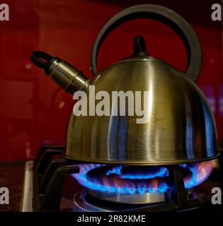 A kettle boiling water on a LPG gas hob. Blue flames licking the side of the kettle. Stock Photo