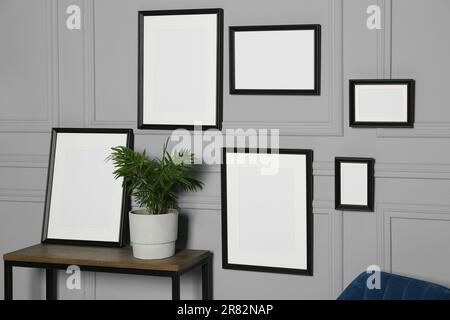 Empty frames hanging on grey wall near wooden table indoors Stock Photo