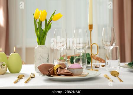 Festive Easter table setting with painted egg, burning candles and yellow tulips indoors Stock Photo