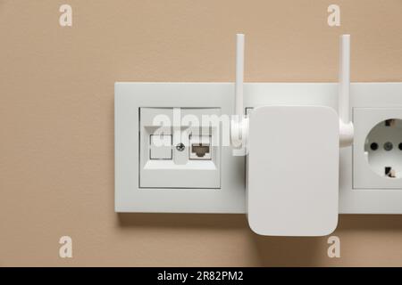 Wireless Wi-Fi repeater in power socket on beige wall Stock Photo