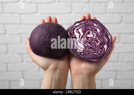 Woman holding dough painted with natural food coloring and red cabbage near white brick wall, closeup Stock Photo