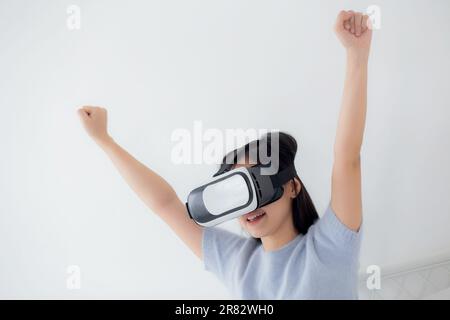 Young asian woman wearing vr headset playing game with excited in the bedroom at home, female using virtual reality or metaverse innovation for simula Stock Photo