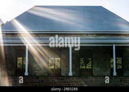 Afternoon sun rays streak across an old stone building in Darwin, Australia. Windows reflect trees not inside the building, but outside. Stock Photo