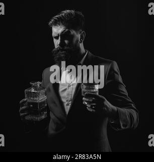 Bartender leather apron holding whisky cocktail in glass. Hipster with beard and mustache in suit drinks alcohol after working day. Stock Photo