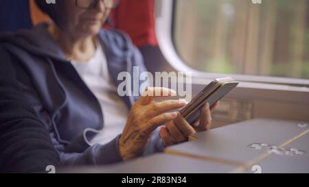 Close-up of the hands of an elderly woman sitting in a train carriageriage and using a smartphone Stock Photo