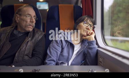 Elderly couple is riding in a train carriage and looking out the window Stock Photo