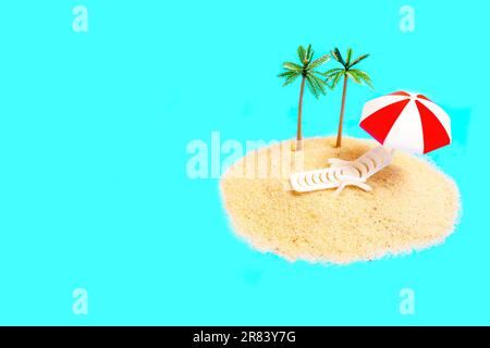Miniature toy composition with a lounge char, sun shade and palm tree figurines placed on a small pile of sand isolated on blue background. Creative T Stock Photo