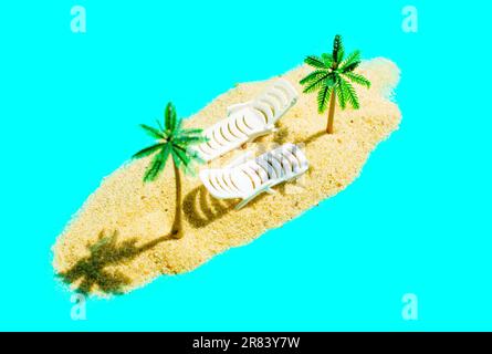 Miniature beach getaway composition with toy palm trees, two white loungers and a sand pile on turquoise blue backdrop. Stock Photo
