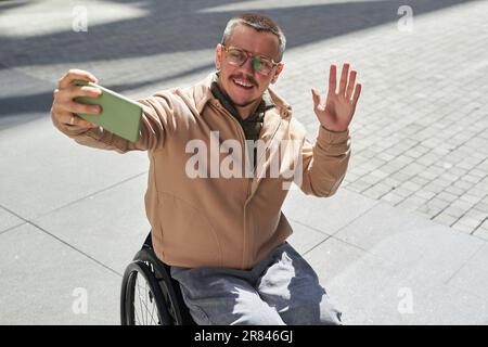 Young man with disability having video call on his smartphone during his walk in the city Stock Photo