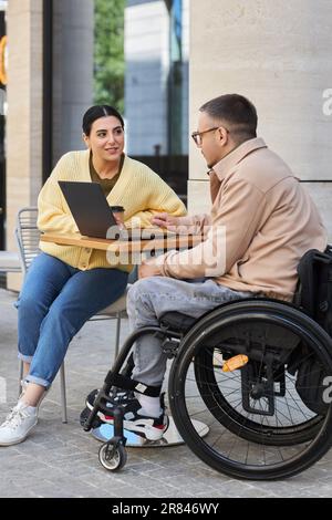 Vertical image of young people having meeting in outdoor cafe, they drinking coffee and using laptop Stock Photo