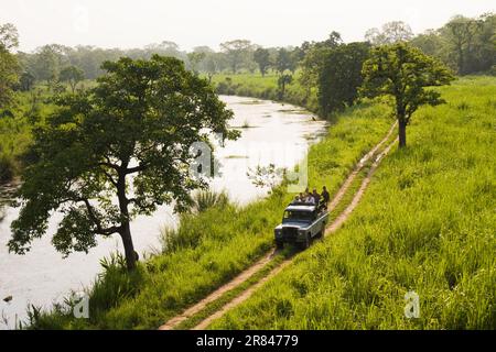 Tourists on a wildlife safari ride in the back of a jeep down a dirt road through Royal Chitwan National Park, Nepal. Stock Photo