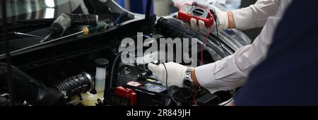 Professional auto mechanic works in a car service and tests operation of engine with tester Stock Photo